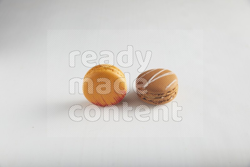 45º Shot of of two assorted Brown Irish Cream, and Orange Exotic macarons on white background