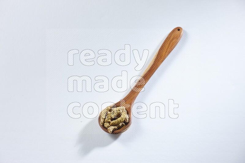 A wooden ladle full of dried turmeric fingers on white flooring
