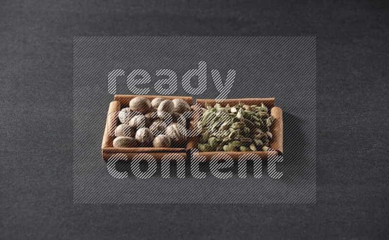 مربعان من أعواد القرفة ممتلئان بجوزة الطيب وحبوب الهيل علي خلفية سوداء