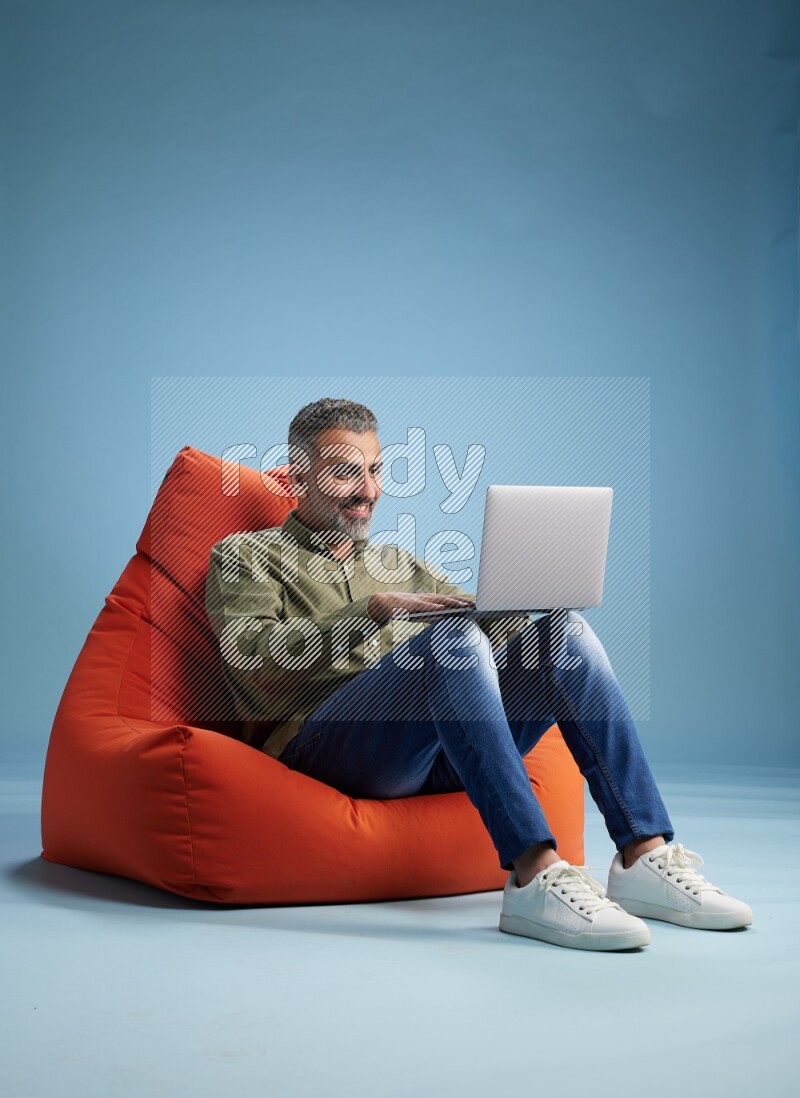 A man sitting on an orange beanbag and working on laptop