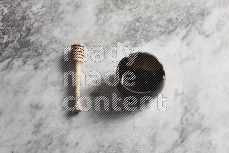Multicolored pottery bowl with wooden honey dipper on the side on grey marble background