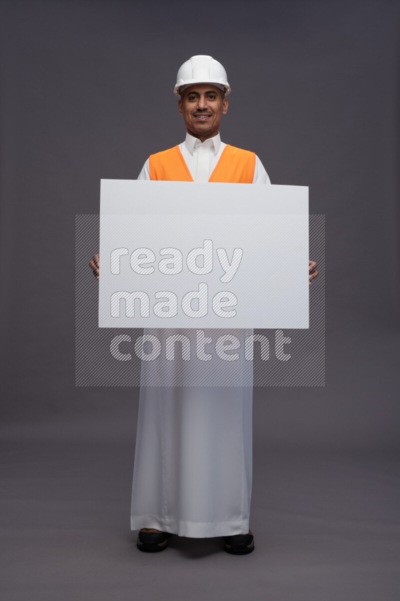 Saudi man wearing thob with engineer vest standing holding board on gray background