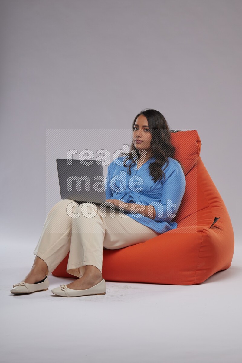 A woman sitting on an orange beanbag and working on laptop