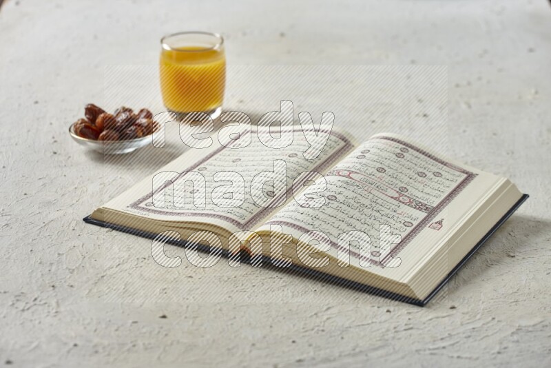 Quran with dates, prayer beads and different drinks all placed on textured white background