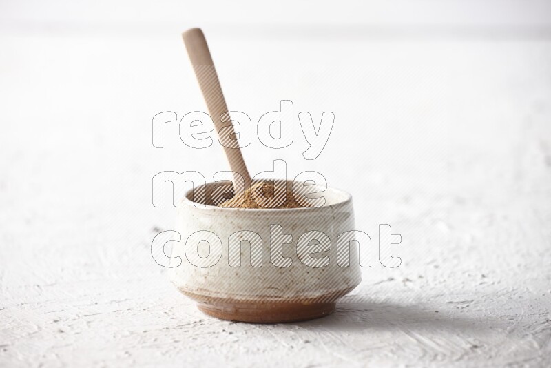 Ceramic beige bowl full of cinnamon powder with a wooden spoon on a textured white background