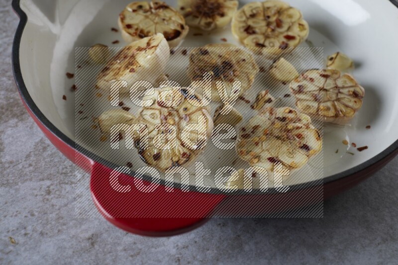 half's roasted garlic in a red-coated cast iron pan on a grey textured countertop