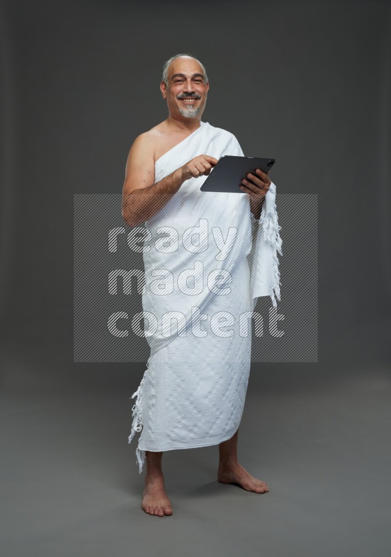 A man wearing Ehram Standing working on tablet on gray background
