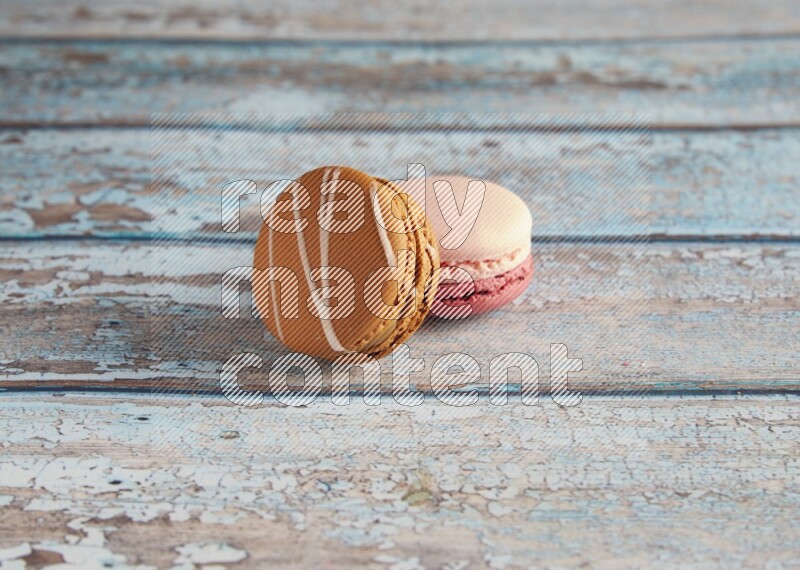 45º Shot of of two assorted Brown Irish Cream, and Pink Litchi Raspberry macarons on light blue background