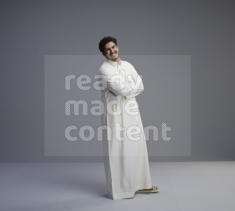 A Saudi man standing wearing thob interacting with the camera on gray background