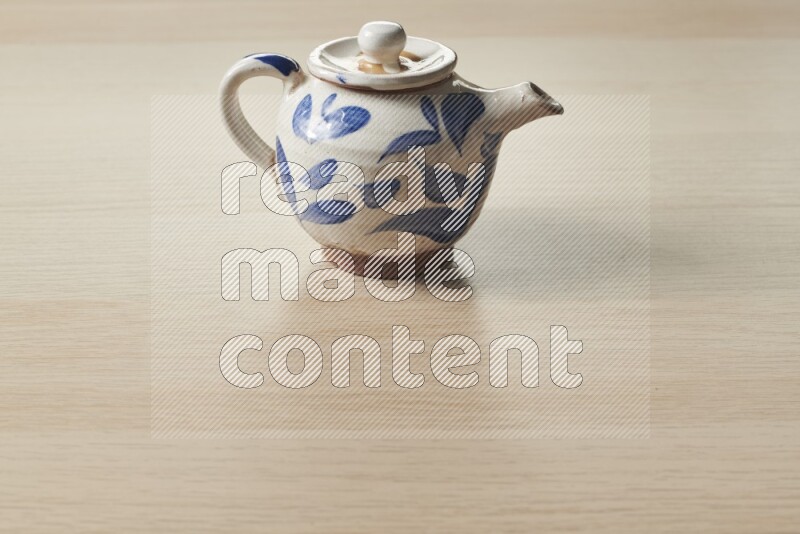 A pottery teapot on light wooden background