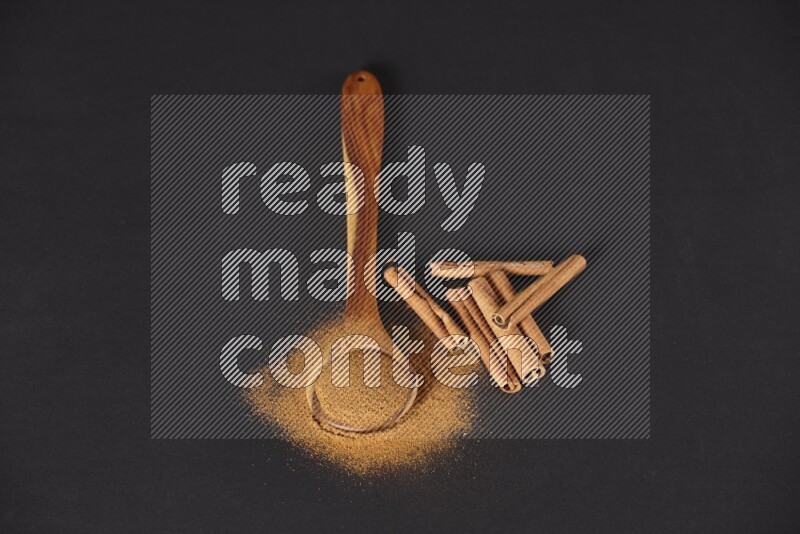 Cinnamon powder in a spoon ladle and spreaded on the floor beside it cinnamon sticks on the floor on black background in different angles