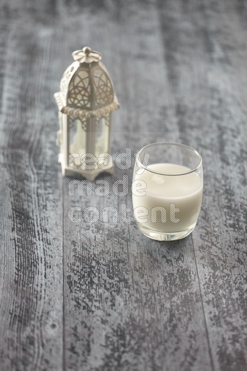 A white lantern with different drinks, dates, nuts, prayer beads and quran on grey wooden background