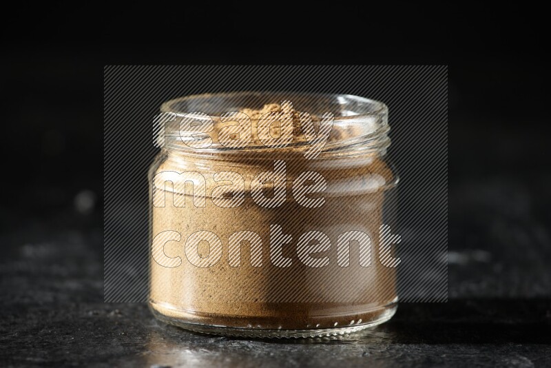 A glass jar full of allspice powder on a textured black flooring