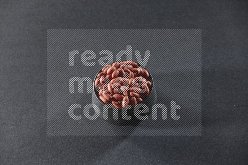 A black pottery bowl full of red skin peanuts on a black background in different angles