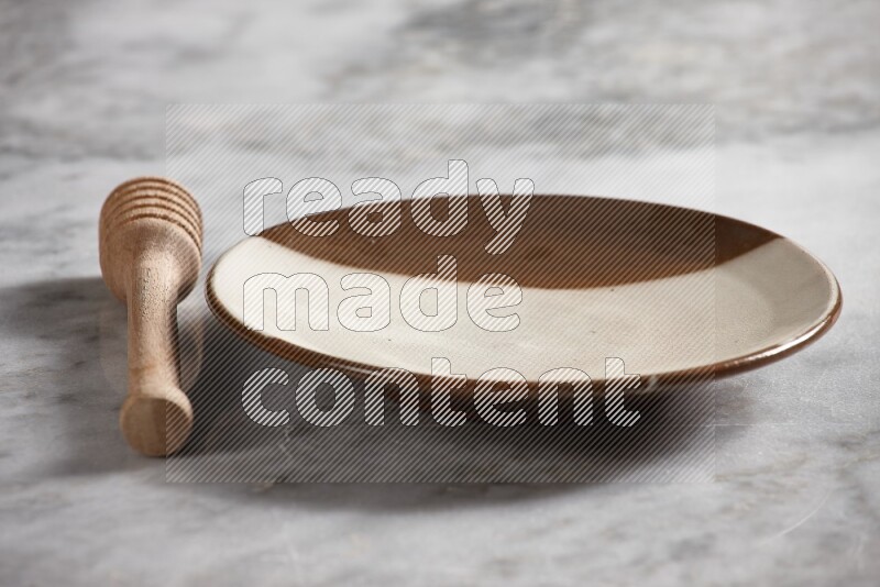 Multicolored pottery plate with wooden honey dipper on the side on grey marble background