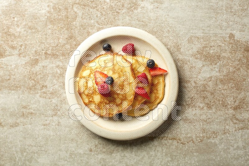 Three stacked mixed berries pancakes in a beige plate on beige background