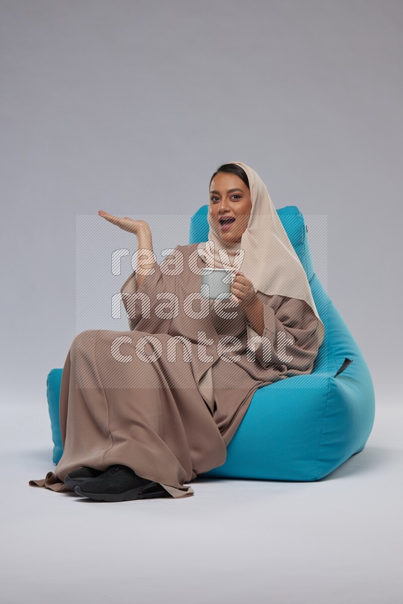 A Saudi woman sitting on a blue beanbag and drinking coffee