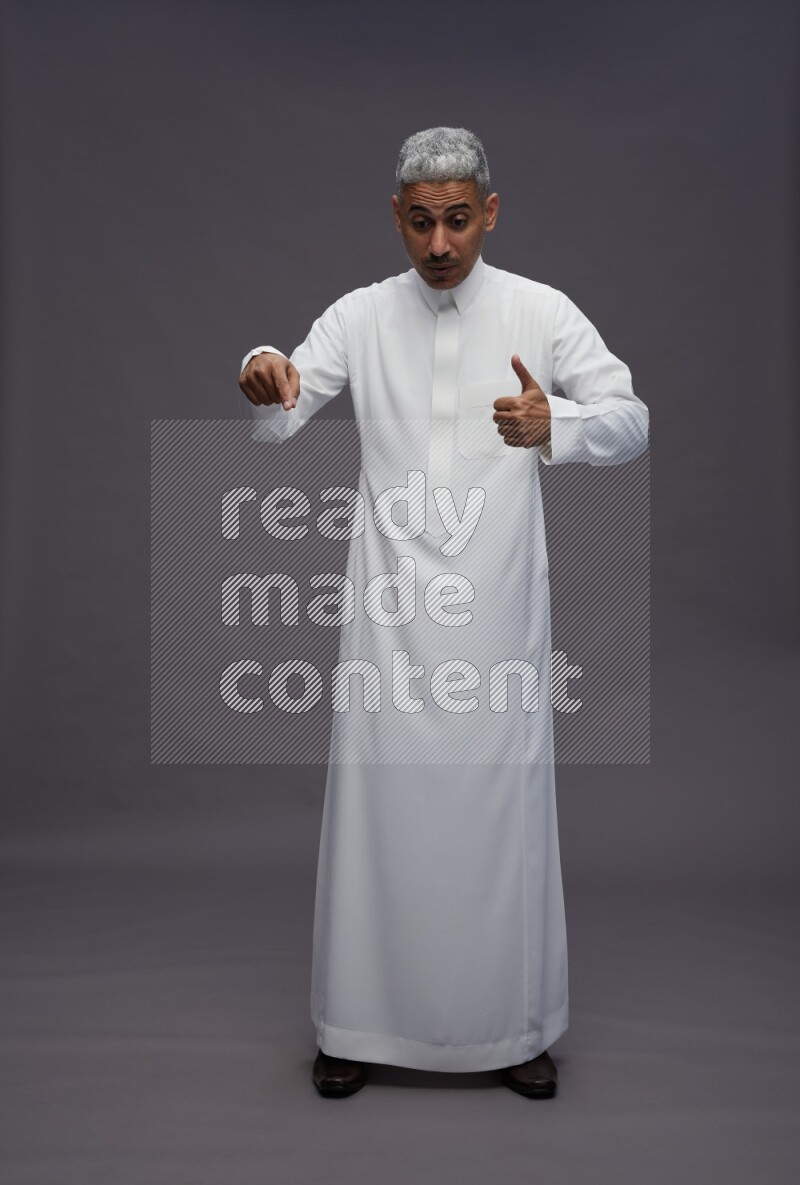 Saudi man wearing thob standing interacting with the camera on gray background