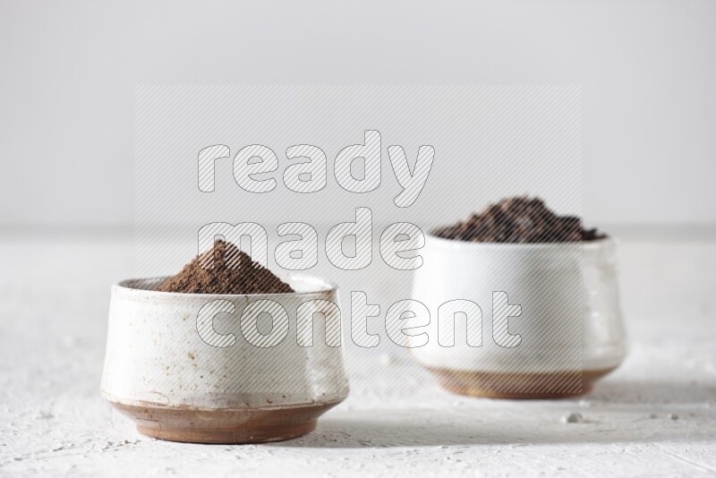 2 Beige ceramic bowls, one full of cloves and the other full of powder on textured white flooring
