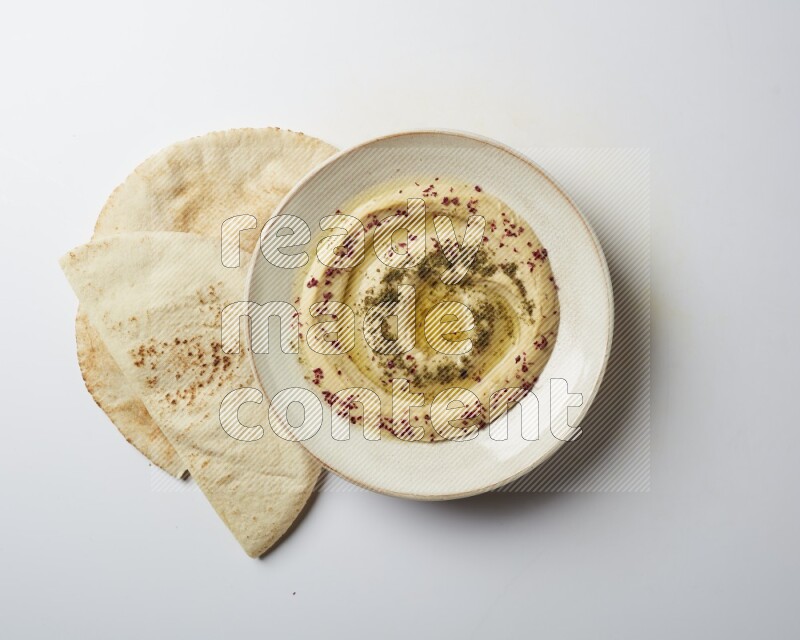Hummus in a pottry plate garnished with zaatr & sumak on a white background
