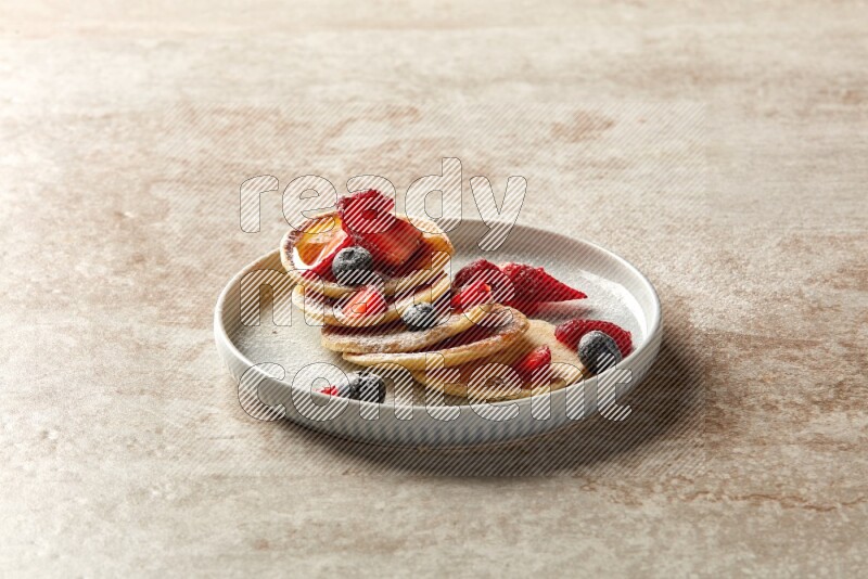 Five stacked mixed berries mini pancakes in a blue plate on beige background