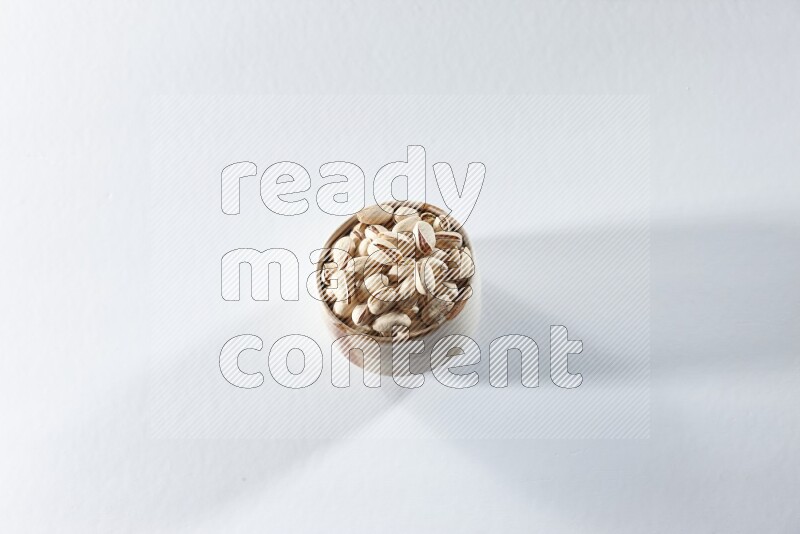 A beige ceramic bowl full of pistachios on a white background in different angles