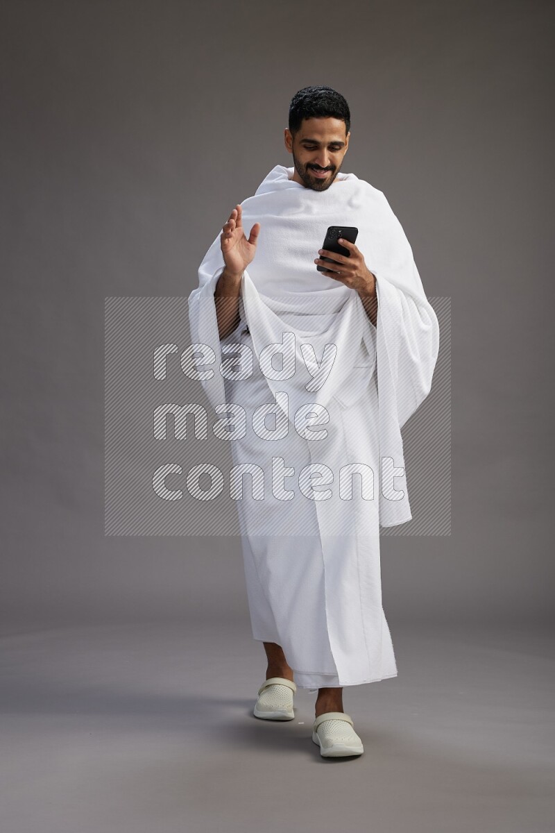 A man wearing Ehram Standing texting on phone on gray background