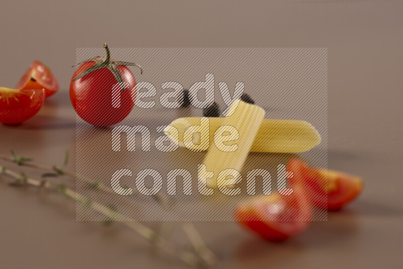Raw pasta with different ingredients such as cherry tomatoes, garlic, onions, red chilis, black pepper, white pepper, bay laurel leaves, rosemary and cardamom on beige background