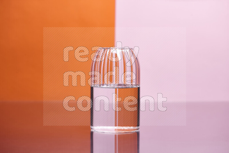 The image features a clear glassware filled with water, set against orange and rose background