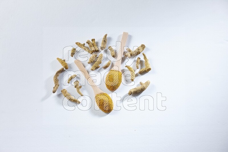 ملعقتان خشبيتان ممتلئتان ببودرة الكركم مع أصابع الكركم المجففة بجانبهما على خلفية بيضاء