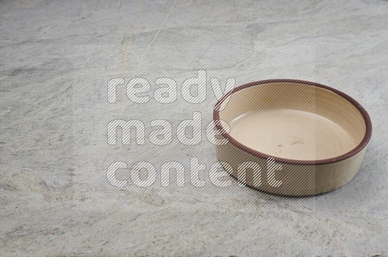 A beige pottery oven bowl on grey marble background