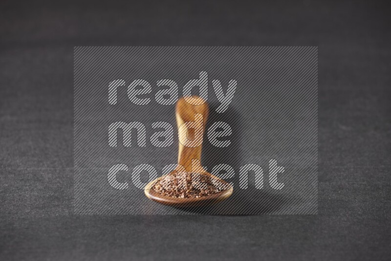 A wooden ladle full of flaxseeds on a black flooring