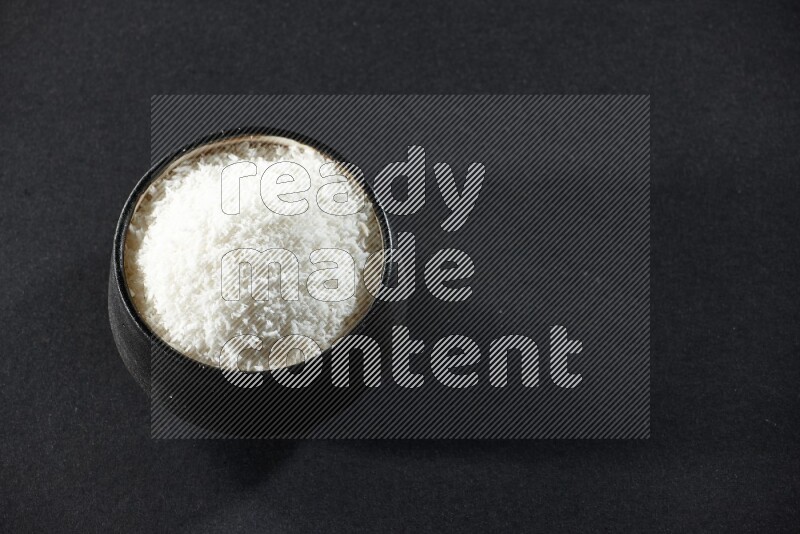 A black pottery bowl full of desiccated coconut on a black background in different angles