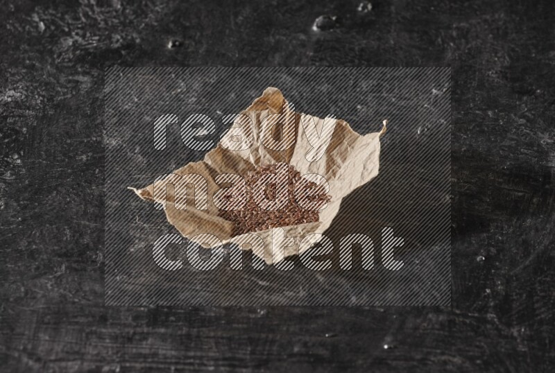 A crumpled piece of paper full of flaxseeds on a textured black flooring