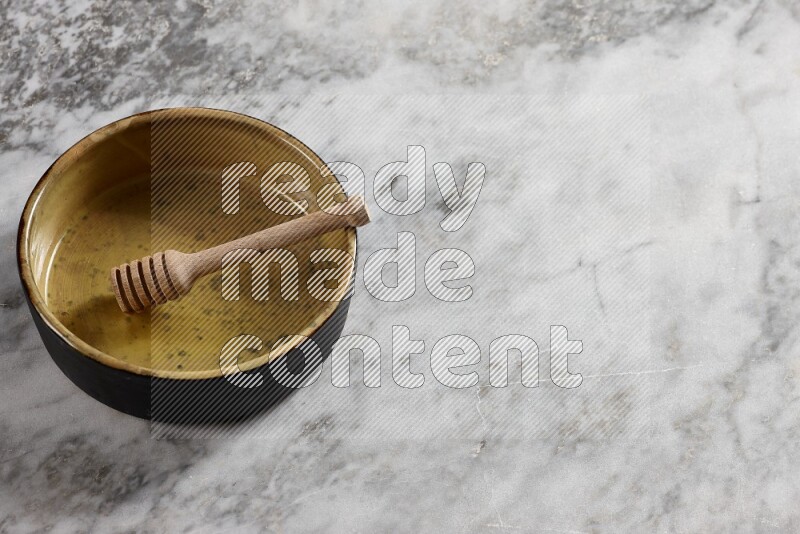 Multicolored pottery oven plate with wooden honey dipper in it on grey marble background