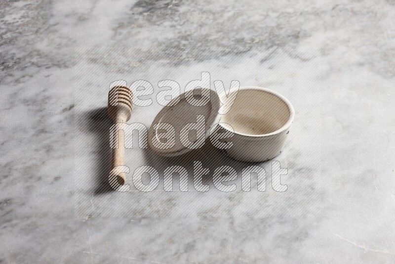 White pottery bowl with wooden honey dipper on the side on grey marble background