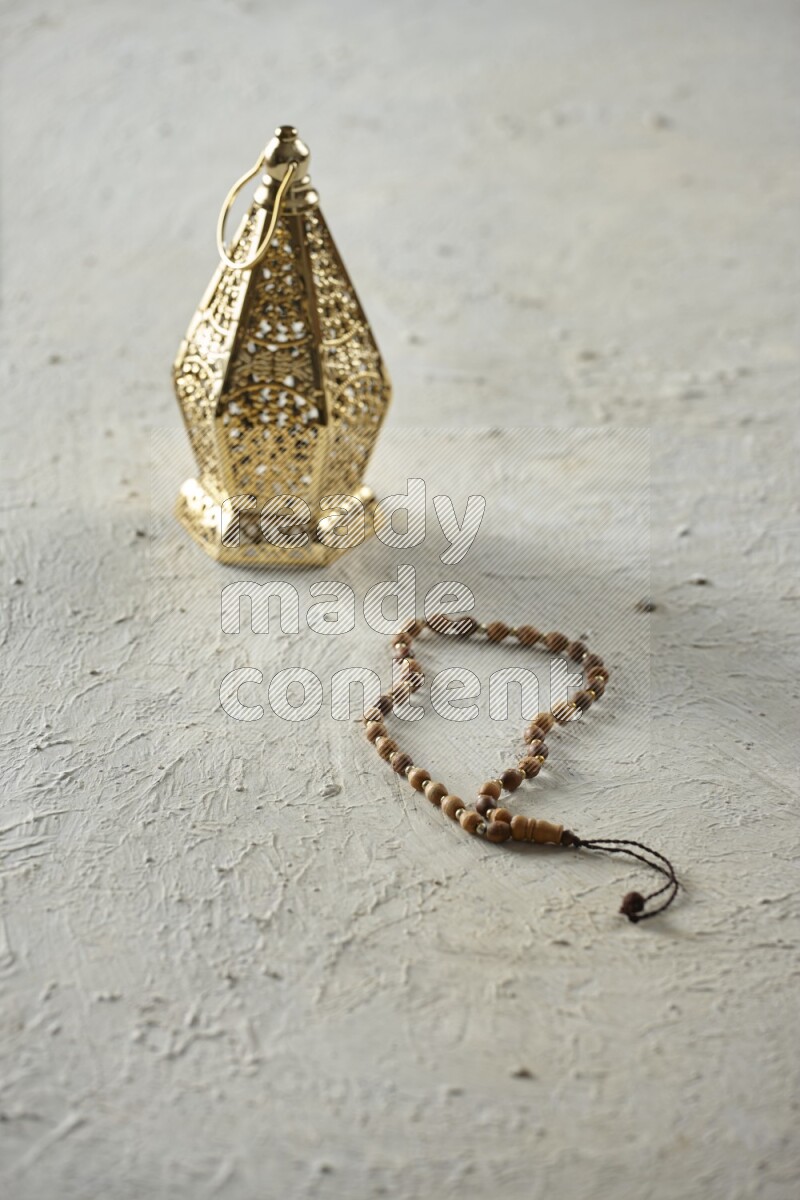 A golden lantern with different drinks, dates, nuts, prayer beads and quran on textured white background
