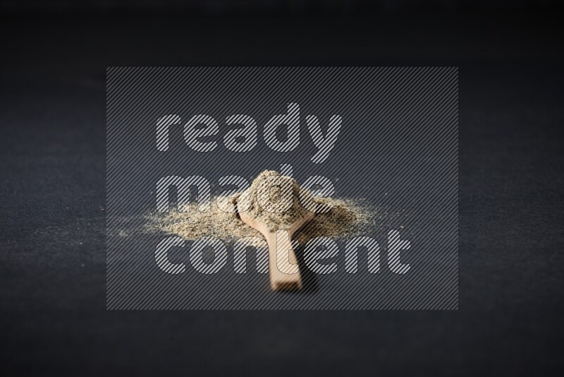 A wooden spoon full of cardamom powder and powder spreaded on black flooring