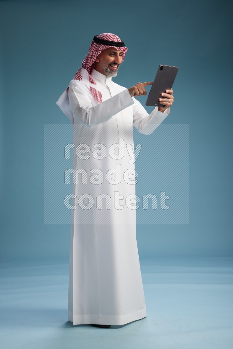 Saudi man wearing thob and shomagh with tablet on Blue background