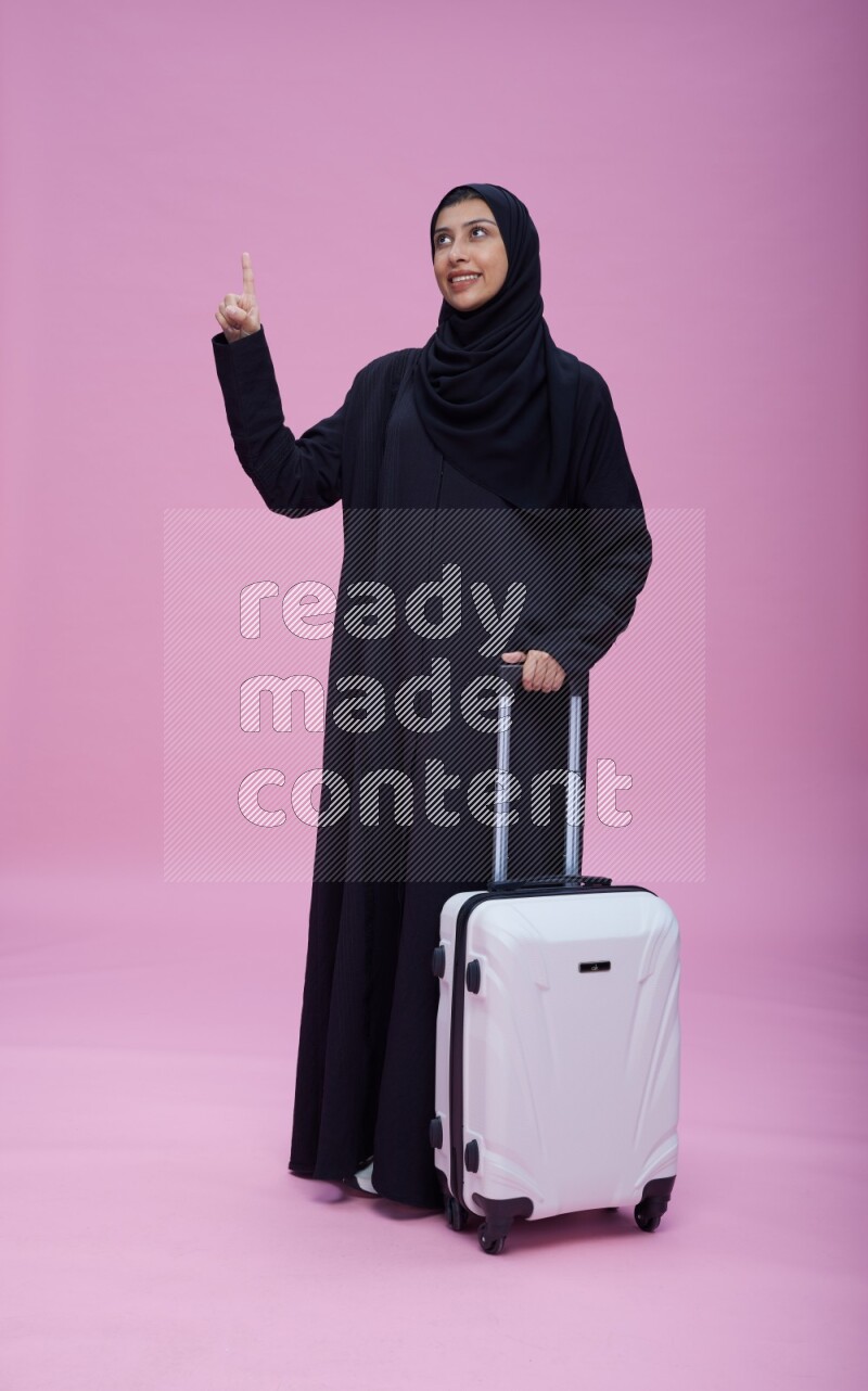Saudi woman wearing Abaya standing holding bag on pink background