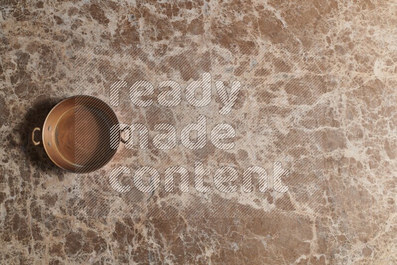 A small copper pan on beige marble background