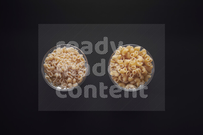 Different pasta types in glass bowls on black background