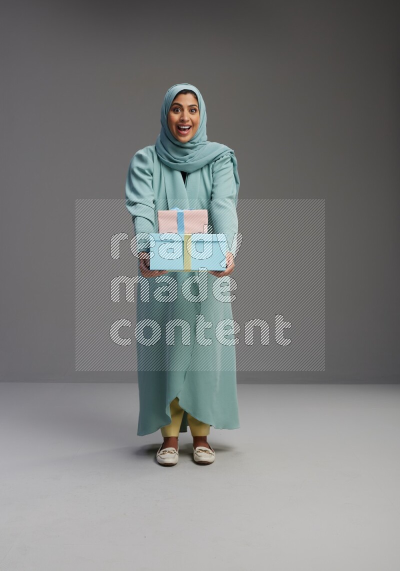 Saudi Woman wearing Abaya standing holding gift box on Gray background