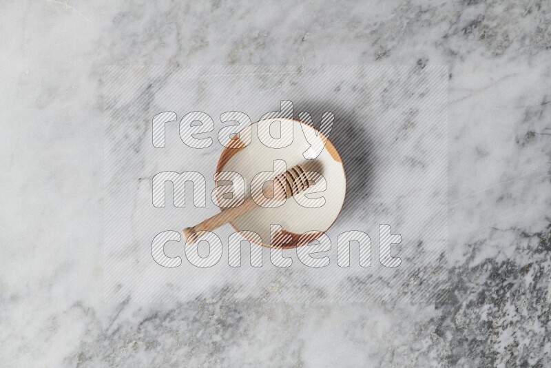 Multicolored pottery plate with wooden honey dipper in it on grey marble background