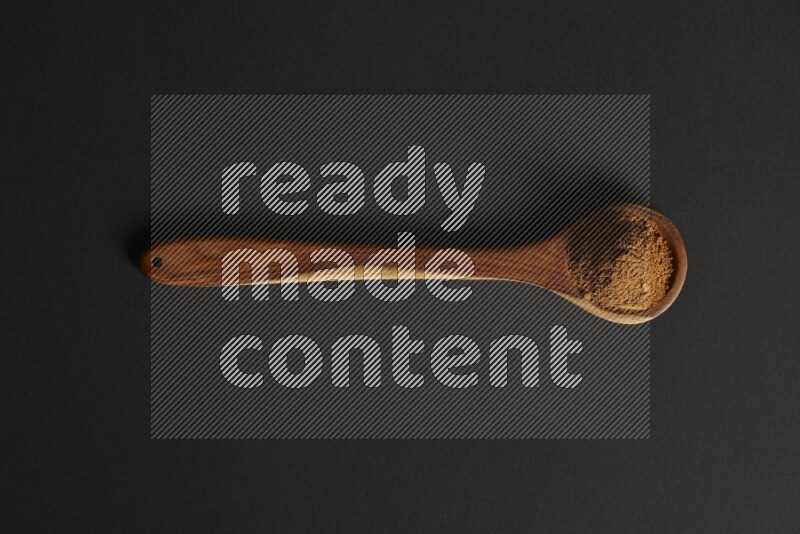 Cinnamon powder in a spoon ladle on black background