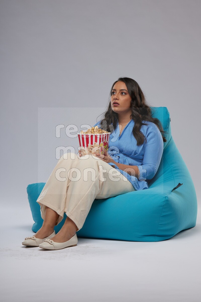 A woman sitting on a blue beanbag and eating popcorn