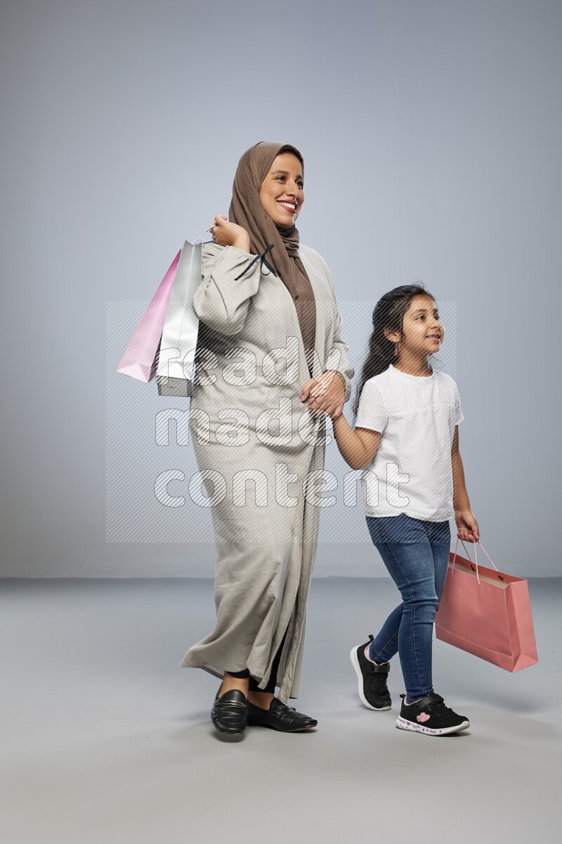 Mom and daughter holding shopping bags on gray background