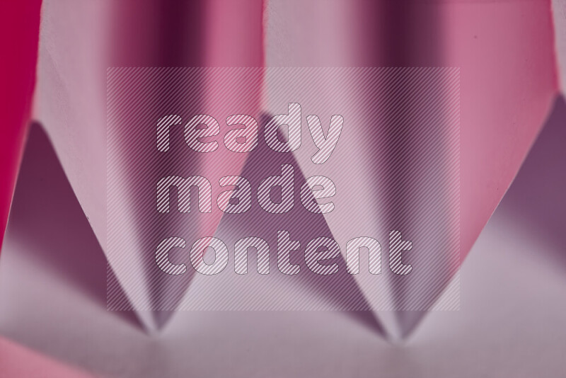 A close-up abstract image showing sharp geometric paper folds in pink gradients