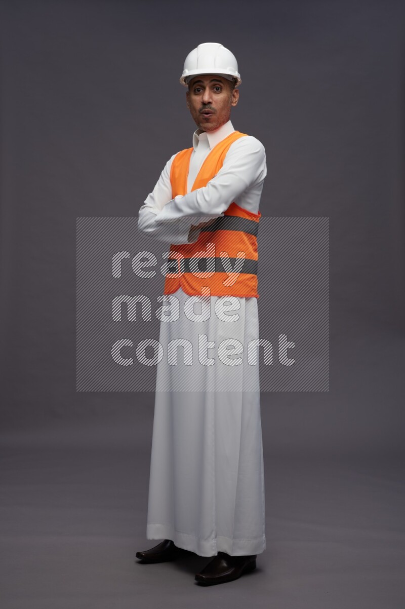 Saudi man wearing thob with engineer vest standing with crossed arms on gray background