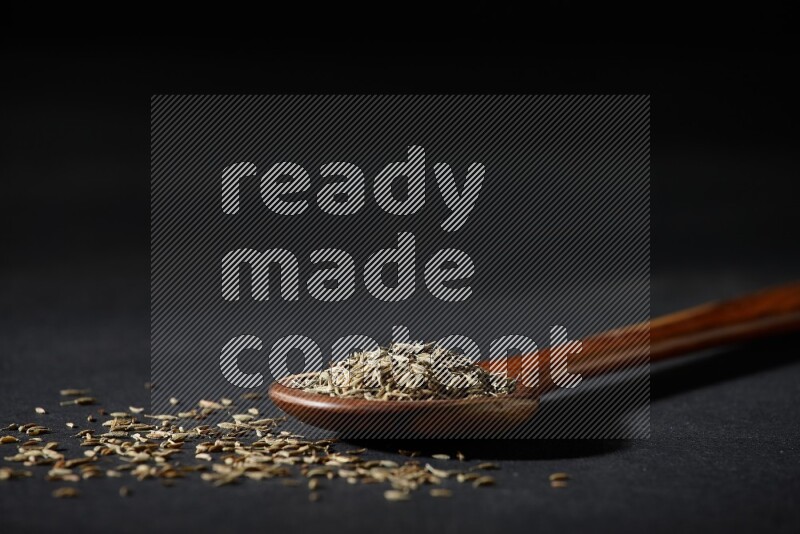 A wooden ladle full of cumin seeds on black flooring